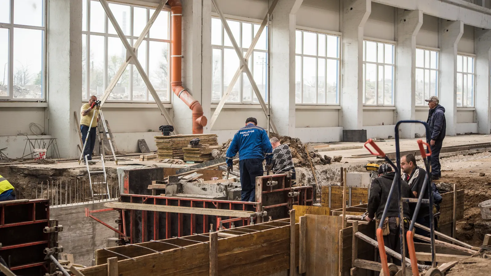 A production hall under construction — formwork, reinforcement and workers beneath the tall windows.